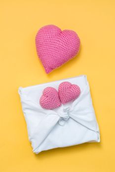 Zero waste valentine's day. Eco friendly gift furoshiki and knitted hearts on yellow background. Vertical view