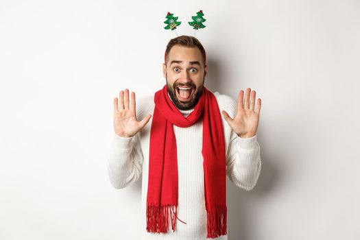 Christmas holidays. Excited bearded man raising hands up and shouting for joy, celebrating New Year party, standing against white background.