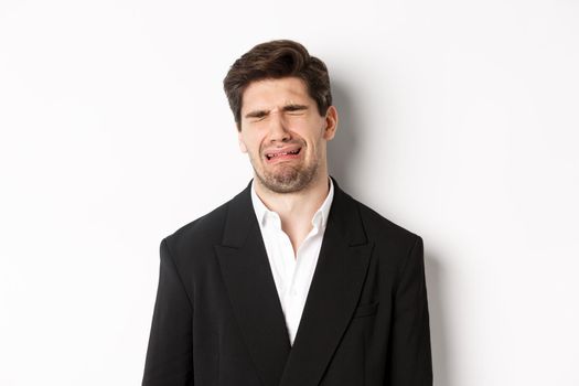Close-up of miserable man in suit, crying and sobbing, feeling sad, standing against white background.