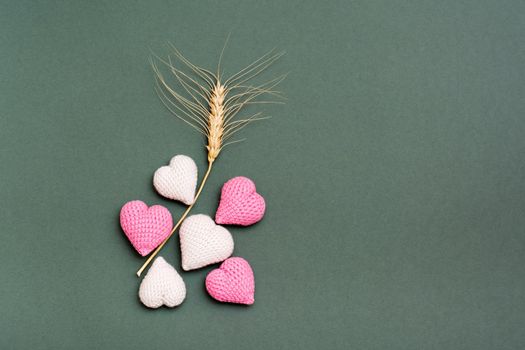 Romantic still life of knitted hearts and an ear of wheat on a green background