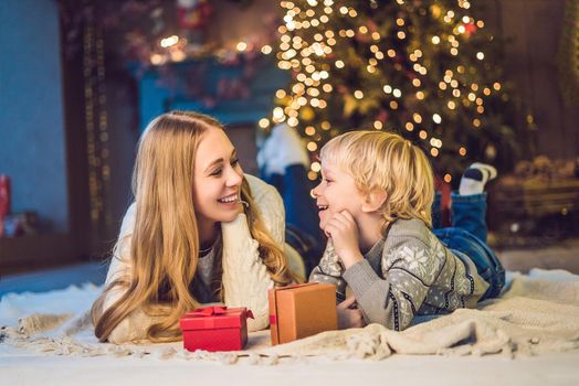 Portrait of happy mother and adorable boy celebrate Christmas. New Year's holidays. Toddler with mom in the festively decorated room with Christmas tree and decorations.