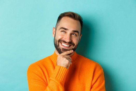 Close-up of caucasian male model having an idea, smiling and looking upper left corner thoughtful, imaging plan, standing over light blue background.