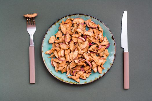 Slices of dry apples on a plate and cutlery on a green background. Healthy eating. Top view