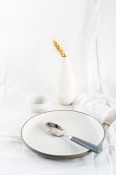 Home serving dishes for eating. Empty plate and spoon on the table on a white cloth. Vertical view