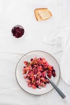 Russian traditional salad with vegetables - vinaigrette on a plate, bread and a bowl of beets on a table on a cloth. Top view. Vertical view