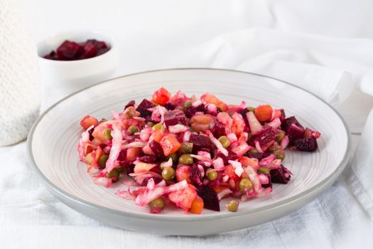 Russian traditional salad with vegetables - vinaigrette on a plate and a bowl of beets on a table on a cloth. Close-up