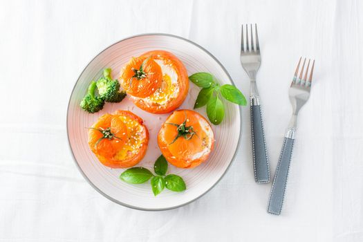 Baked tomatoes with egg and basil leaves on the table. Diet lunch. Top view