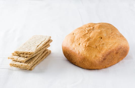 Concept of choice between fresh loaf of wheat homemade bread and cereal crispbread on white cloth