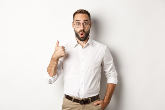 Impressed young male entrepreneur showing thumbs-up, praise something good, like and agree, white background.