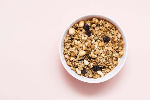 Healthy eating. Baked oats, nuts and raisins granola in a bowl on a pink background. Top view