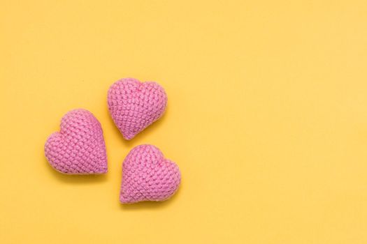 Handmade for Valentine's Day. Three knitted pink hearts on a yellow background. Copy space