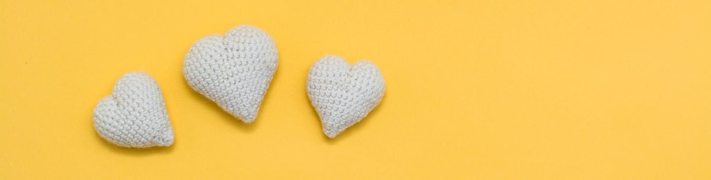 Handmade for Valentine's Day. Knitted white hearts on a yellow background. Web banner