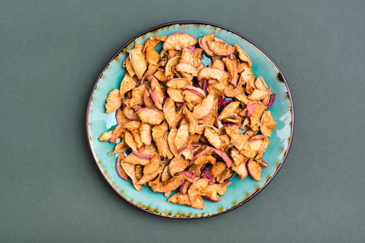 Pieces of dry apples on a plate on a green background. Healthy eating. Top view