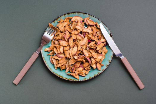 Slices of dry apples on a plate and cutlery on a green background. Healthy eating