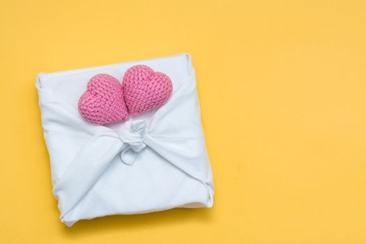 Zero waste valentine's day. Eco friendly gift furoshiki and knitted hearts on yellow background. Copy space. Top view