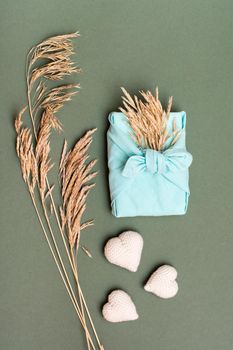 Eco friendly valentine's day gift furoshiki, knitted hearts and ears of dry grass on green background. Vertical view