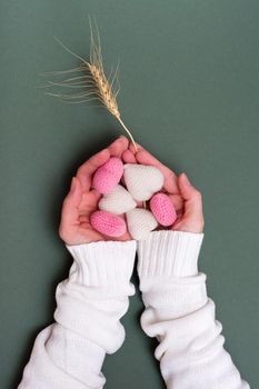 Still life for Valentine's Day. Knitted hearts in female hands and an ear of wheat on a green background. Vertical view