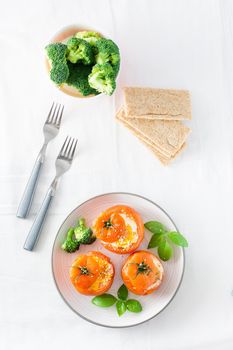 Baked tomatoes with egg, broccoli and basil leaves on a plate. Diet lunch. Top view. Vertical view