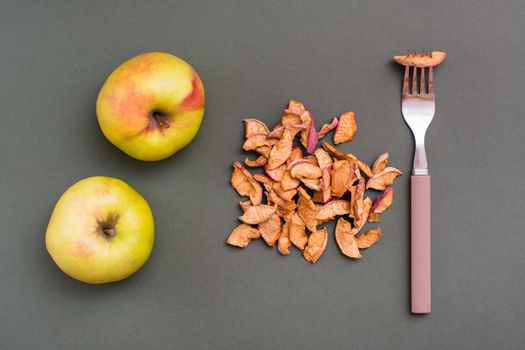 A handful of pieces of dry apples, a fork and fresh apples on a green background. Healthy eating