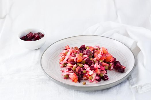 Russian traditional salad with vegetables - vinaigrette on a plate and a bowl of beets on a table on a cloth