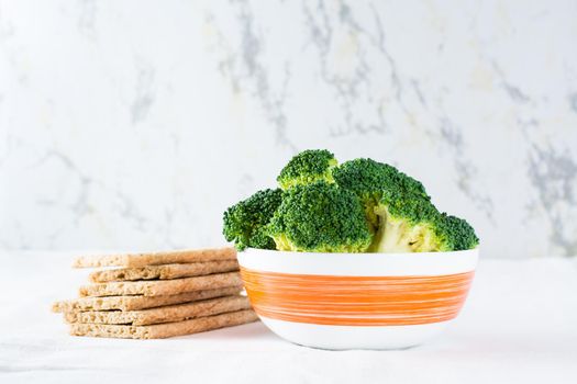 Fresh broccoli in a bowl and grain crispy bread on a table on a cloth. Copy space