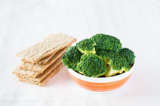Fresh broccoli in a bowl and grain crispy bread on a table on a cloth