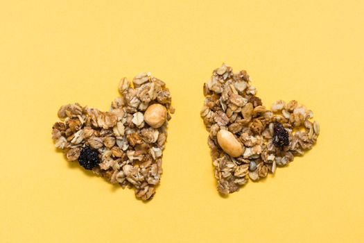 Love for healthy food. Granola made from oats, nuts and raisins in the form of two hearts on a yellow background. Top view