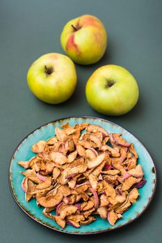 Slices of dry apples on a plate and fresh apples on a green background. Healthy eating. Vertical view