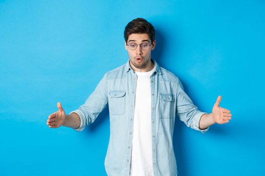 Excited handsome man showing big size object and looking amazed, standing over blue background.