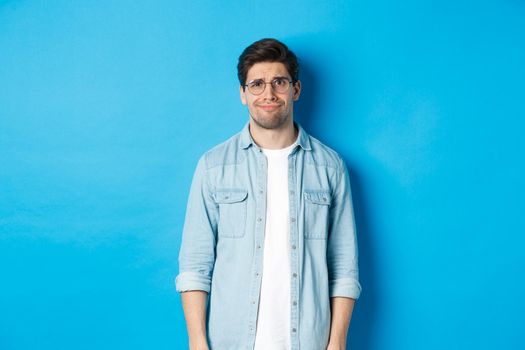 Skeptical and doubtful guy in glasses, looking confused at something strange, blue background.