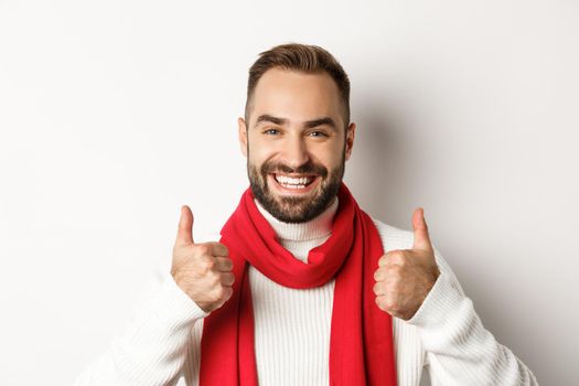 Christmas holidays. Handsome satisfied guy showing thumbs up, like and approve, enjoying great winter holidays, white background.