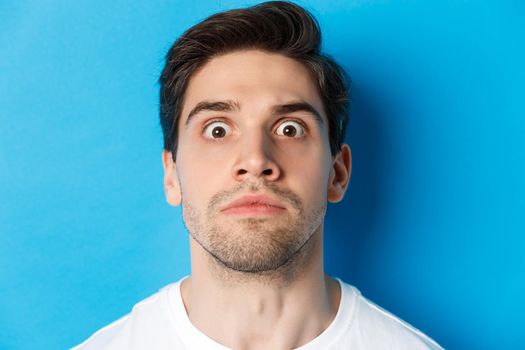 Headshot of pissed-off man losing his temper, looking tensed and angry, standing over blue background. Copy space