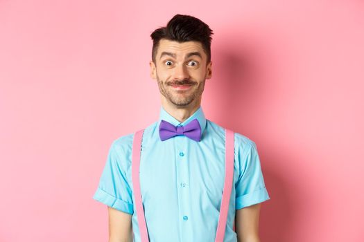 Smiling caucasian man looking excited, standing in classy bow-tie and shirt for romantic date, pink background.