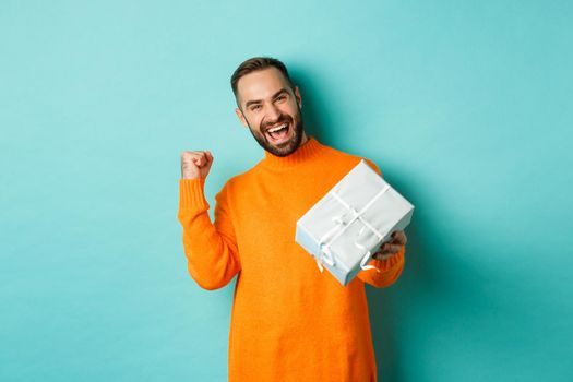 Holidays and celebration concept. Excited man receiving gift, looking happy at present and smiling, standing over blue background.