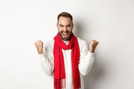 Christmas holidays and New Year concept. Happy man celebrating victory, winning and making fist pumps, achieve goal, saying yes while standing over white background.