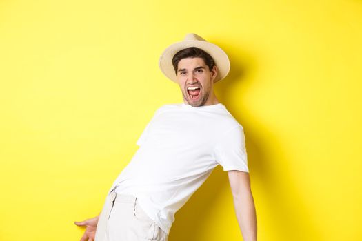 Concept of tourism and vacation. Excited young man tourist celebrating, shouting for joy and dancing, standing over yellow background.