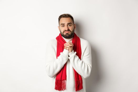 Christmas holidays and New Year concept. Sad man begging for help, holding hands in pray and looking distressed at camera, asking for favour, standing over white background.