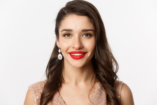 Concept of New Year celebration and winter holidays. Headshot of beautiful young woman with red lips, wearing luxury earrings, smiling happy at camera, white background.