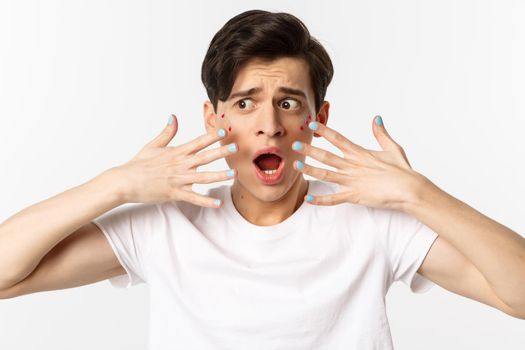 People, lgbtq and beauty concept. Close-up of gay man panicking, showing nail polish on hands, looking alarmed and worried, standing over white background.