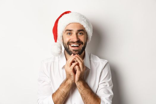 Party, winter holidays and celebration concept. Excited and hopeful man in santa hat looking at christmas gift with amazement, white background.