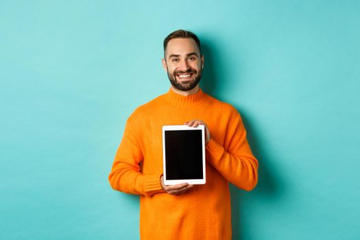 Technology. Smiling handsome man showing digital tablet screen, demonstrating application, standing over turquoise background.