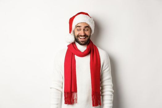 Winter holidays and New Year party concept. Man looking intrigued to the left, wearing Santa hat and celebrating Christmas, standing over white background.