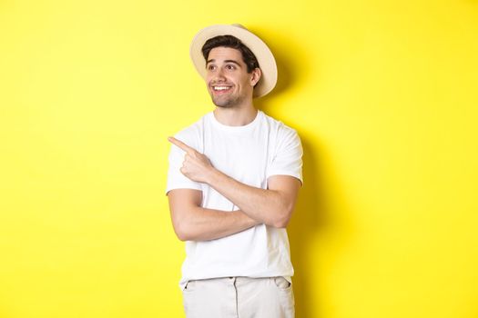 Concept of tourism and lifestyle. Happy man tourist checking out promo, looking pleased and pointing finger at upper left corner logo, yellow background.