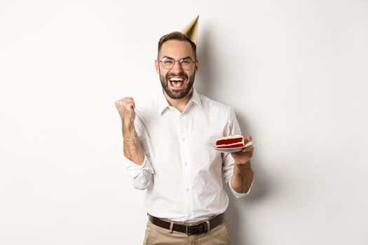 Holidays and celebration. Birthday guy making wish on bday cake and rejoicing, making fist pump sign as winning, achieve goal, white background.