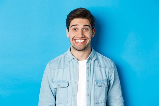 Close-up of smiling excited man with beard, looking amused at advertisement, standing against blue background.