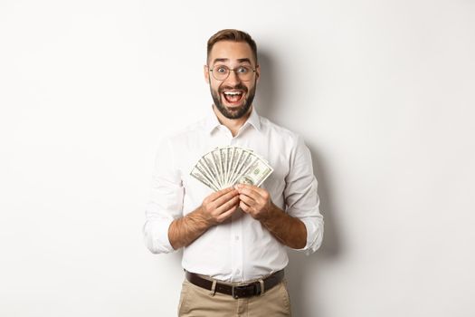 Excited handsome man holding money, rejoicing of winning cash prize, standing over white background.