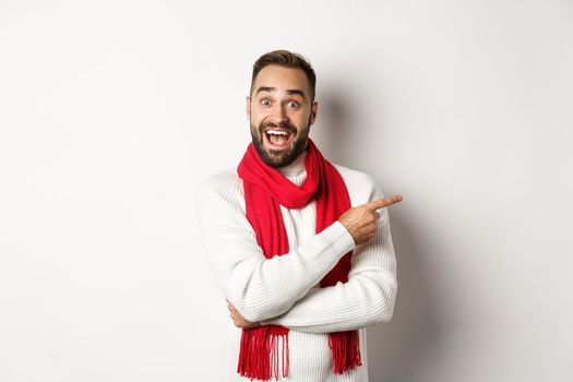 Christmas holidays and celebration concept. Excited bearded male buyer showing your logo, pointing finger right at promo offer, standing against white background.