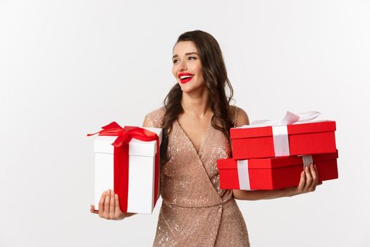 Holidays, celebration concept. Elegant woman with red lips, luxury dress, holding Christmas presents and smiling, enjoying New Year eve, white background.