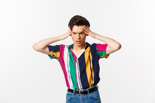 Anxious young gay man standing in panic, holding hands on head and staring down troubled, having a problem, standing over white background.