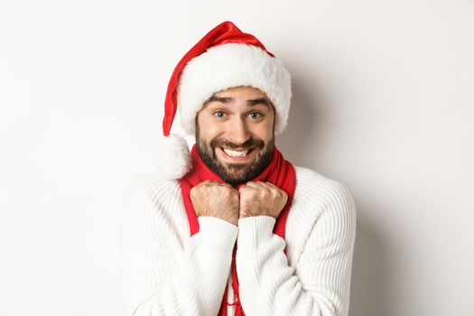 New Year party and winter holidays concept. Handsome guy in Santa hat feeling excited about Christmas, standing amused against white background.